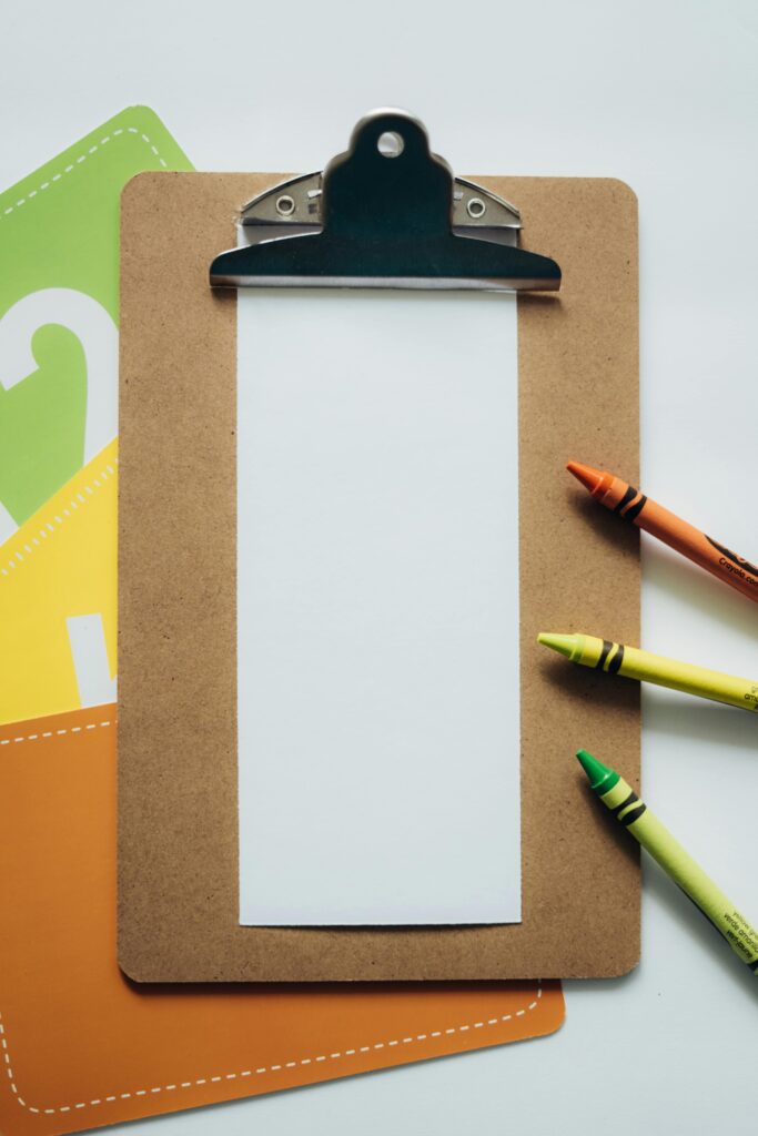 Top view of a clipboard and crayons on a white background, ideal for education themes.